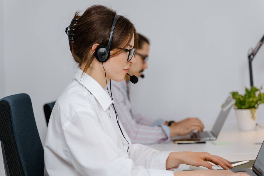 Person wearing headset working on a laptop at a desk in an office setting.