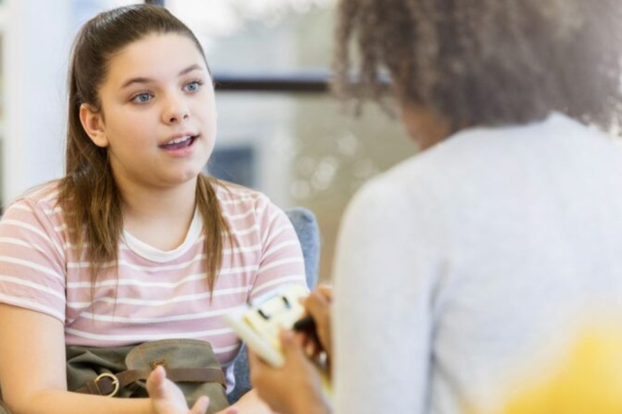 Person taking notes while speaking with another person indoors.