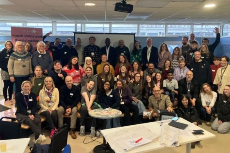 A large group of people stood and sat facing the camera smiling - attendees at Youth Voice Saturday