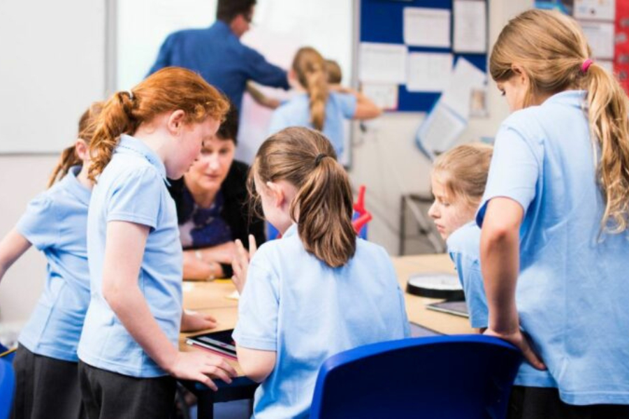 Children in blue school uniforms working together at a classroom table with tablets.