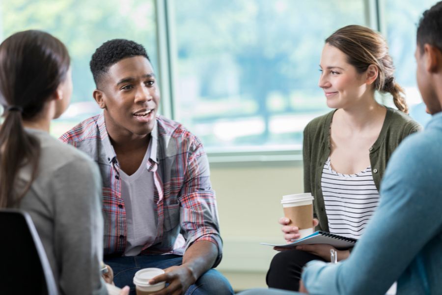 Young adults talking to each other in a circle, holding coffee cups and smiling
