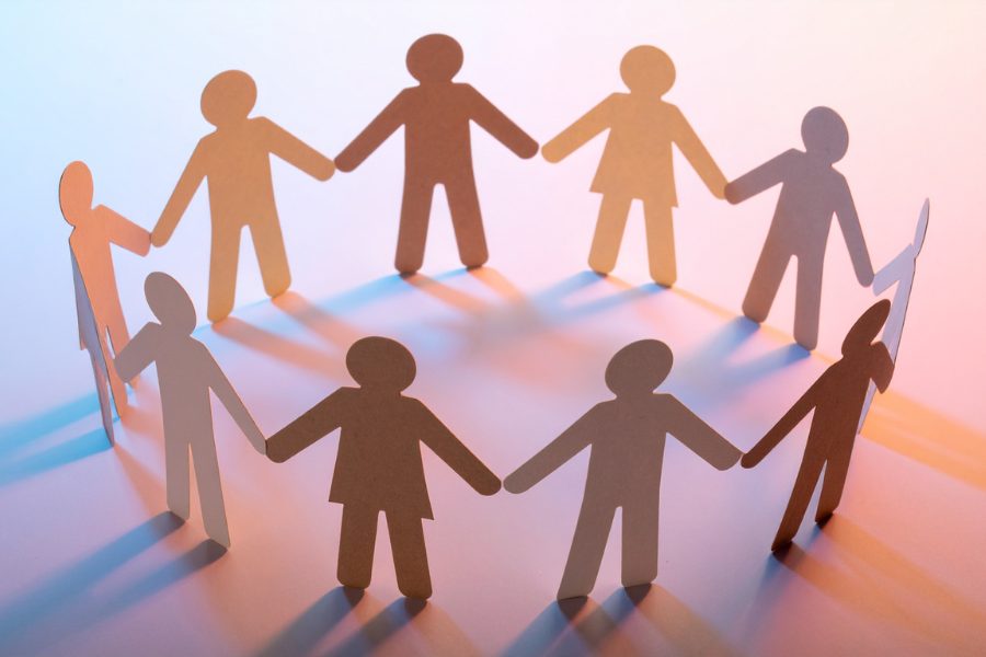 Paper cut-out figures in a circle holding hands, symbolizing unity and collaboration on a gradient background.