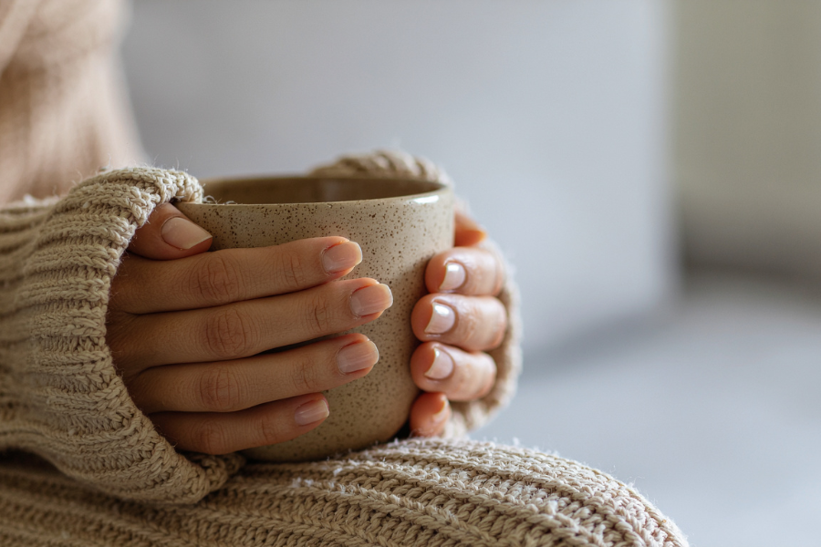 Hands in a cozy knitted sweater holding a warm ceramic mug.
