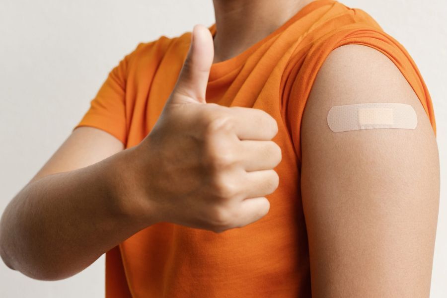 A man holding his thumb up. He's had a flu vaccination in his upper arm. 