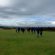 Group of people walking across a grassy field towards the horizon on an overcast day.