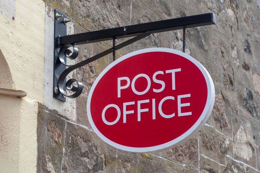 A post office sign hanging from a wall outside a post office