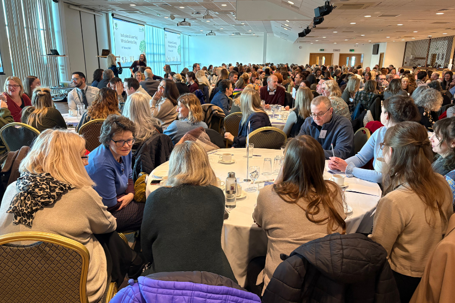 Large group of colleagues seated at round tables during an Inclusion and Learning event in a conference hall.