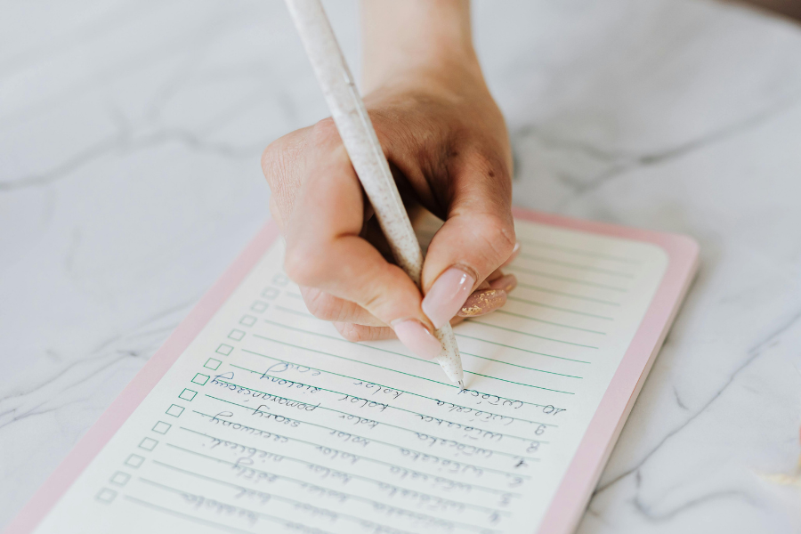 Hand writing on a lined checklist notepad on a table.