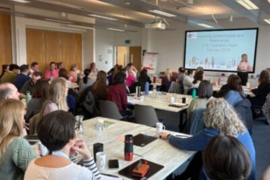 A group of people sat around tables at a conference paying attention to the front of the conference room