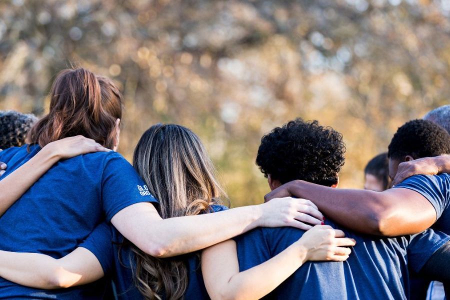 Young people stood side by side with their backs to the camera. They have their arms around each other's shoulders