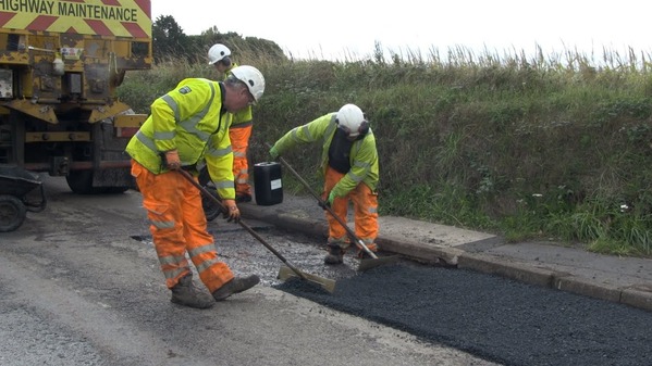 Two road engineers wearing high vis clothing and repairing a road