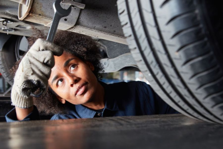 A young person working as a mechanic in a garage, inspecting under a car