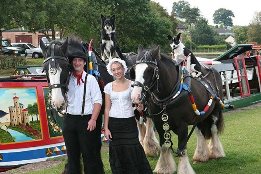 Two members of the Brind family stood in traditional canal-type costume with their horse, in front of a narrowboat.