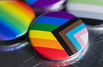 A circular badge depicts the progress Pride flag