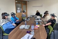 An image shows staff sitting around a conference table, each wearing a VR headset