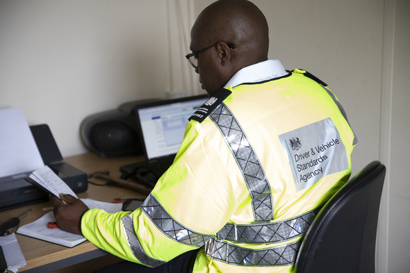 Man sitting at desk working on a laptop. He is wearing a hi-vis jacket