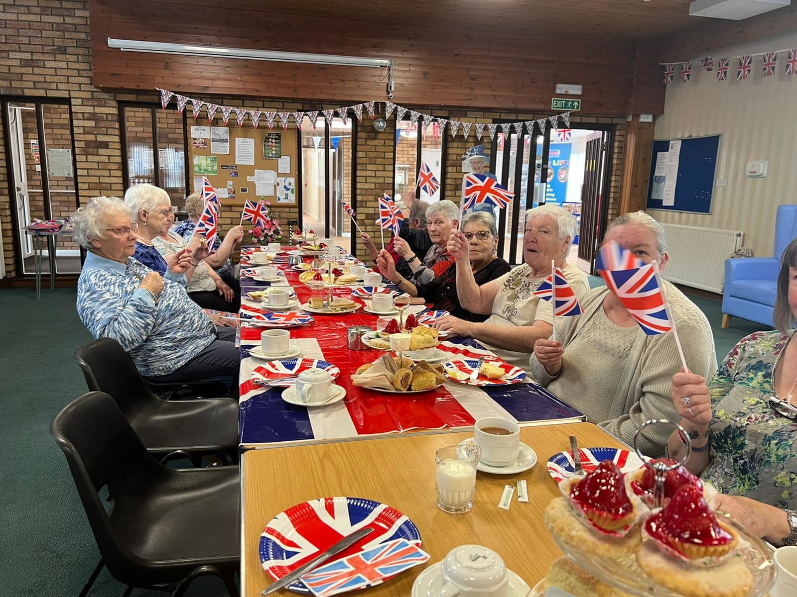 Older ladies enjoying afternoon tea while waving union flags