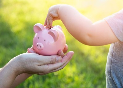 Parent holding a small pink piggy bank as a child places a coin inside