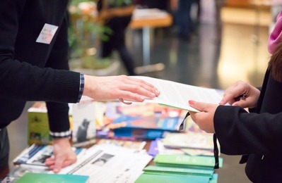 Two people's hands shown gesturing over a table covered in leaflets