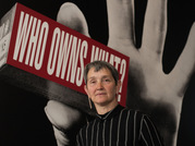 Frances Morris standing in front of a picture of a massive hand holding a sign saying 'Who owns what'