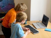 Two children standing at a desk with a keyboard and laptop