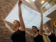 Three female dancers carrying a piece of patterned material above their heads in RAMM's courtyard