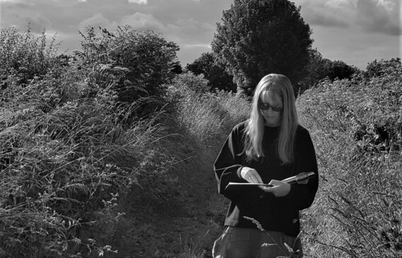 Black and white photo of artist Wendy Rhodes sketching in a rural lane