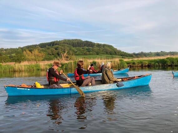 Photo of two rowing boats with people in, on the water, with hills in the background