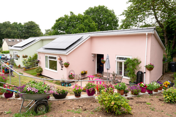 Photo of a pink bungalow with solar panels on the roof and plant pots in the garden