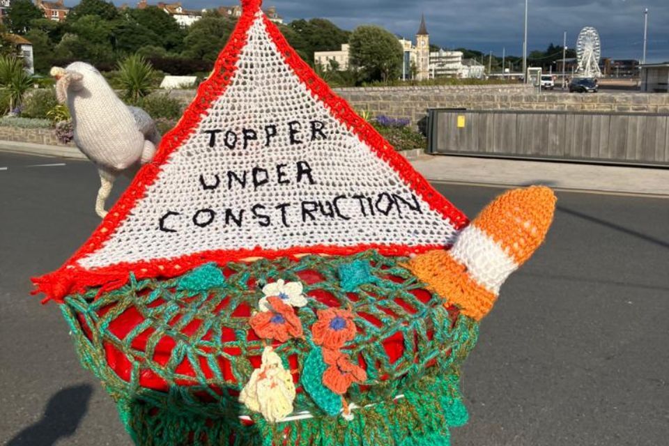 Photo of a crochet postbox topper in Exmouth with a seagull, construction sign and cone