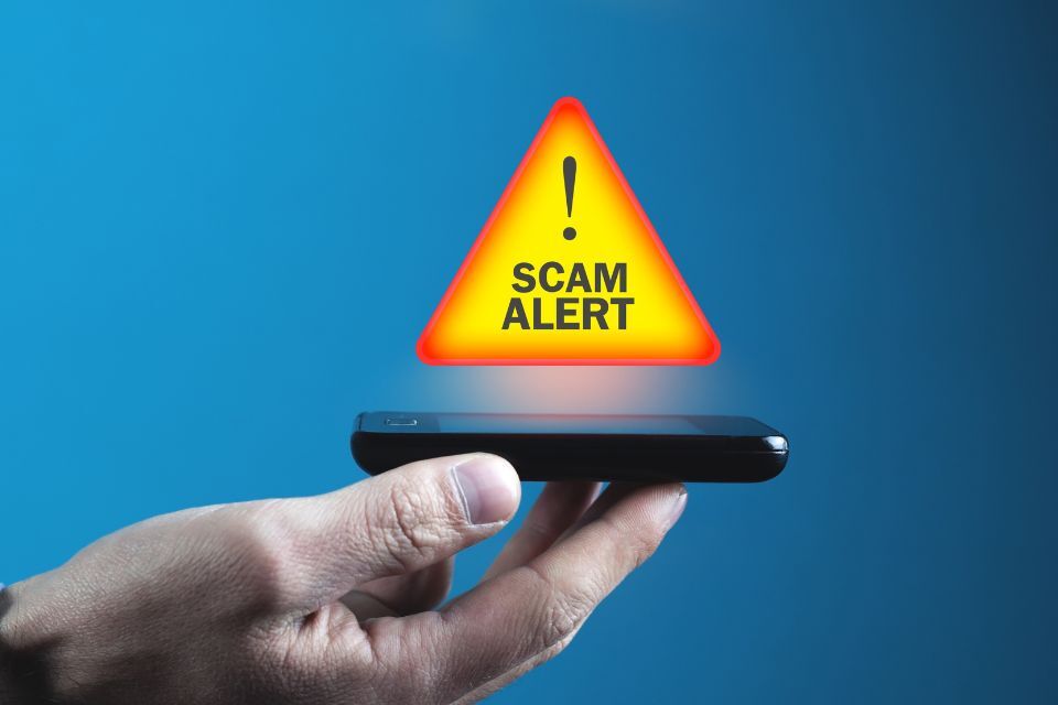 Scam alert warning hovering over a phone being held in a hand