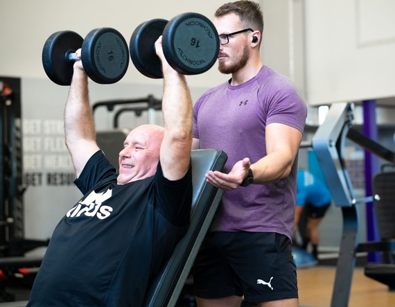 Photo of a person lifting weights and a spotter behind
