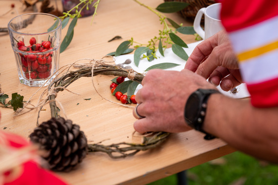 Someone making a Christmas wreath on a wooden table with rose buds, a pinecone and bay leafs