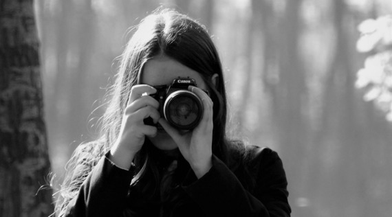 Black and white photo of a person holding a dslr camera to their face, with a blurred background