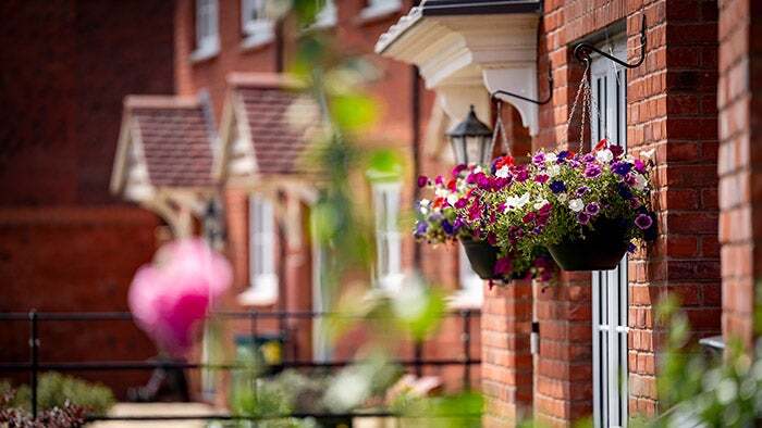 Photo of a row of new homes with baskets of flowers hanging from next to the doorway of the house in the foreground