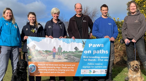 Photo of the Pebblebed Heaths team with 2 dogs and a 'paws on paths' banner
