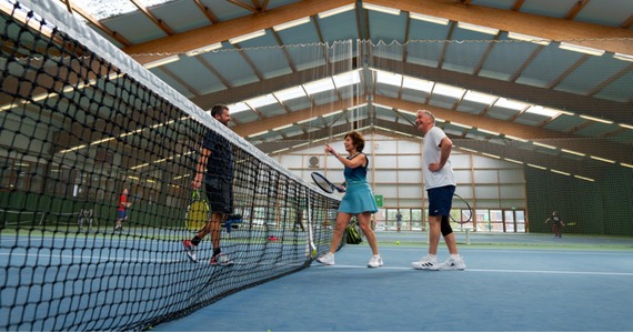 Photo of people with rackets next to a tennis net indoors 
