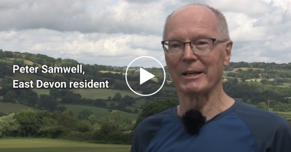 Play button. Peter Samwell, East Devon resident, speaks to the camera, with the Blackdown Hills in the background