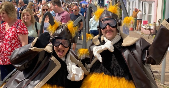 A couple of people dressed up as bees, at Gate to Plate, on a busy Honiton High Street