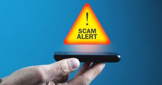 Scam alert in a warning symbol above a phone in a hand