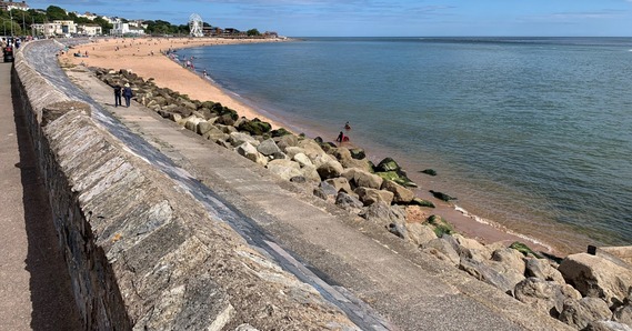 Exmouth Seafront with the seawall on the left, rocks and sea on the right, and seafront buildings in the background