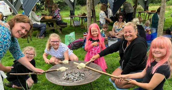 Children and adults gather around with marshmallows on sticks