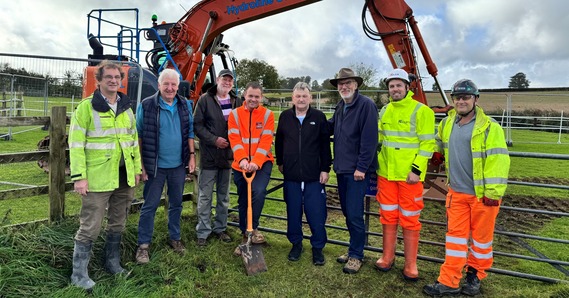 East Devon District Councillors, staff and contractors in high vis jackets, in front of a digger