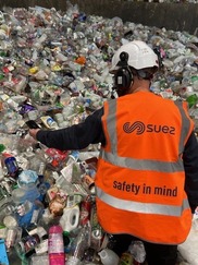 Person wearing a hi-vis jacket and helmet next to a pile of recycling