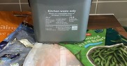 A kitchen waste caddy surrounded by plastic food packaging bags