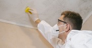 Person wearing gloves and a mask cleaning mould off a ceiling