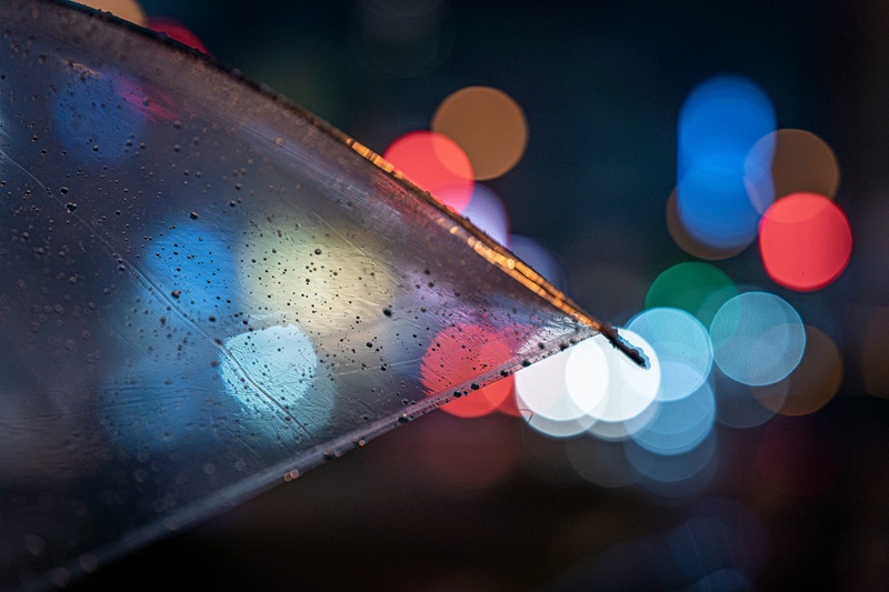 A rainy scene with an umbrella and Christmas lights in the background