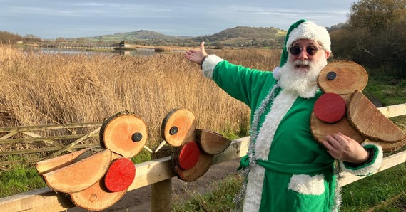 Councillor Loudoun dressed as green santa with wooden robins at Seaton Wetlands