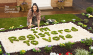 A young disabled woman is in her front garden, crouching over a flower bed. In the flower bed she has spelt out “I’m Registered To Vote” in grass