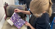 A child holding a printed design above some art equipment